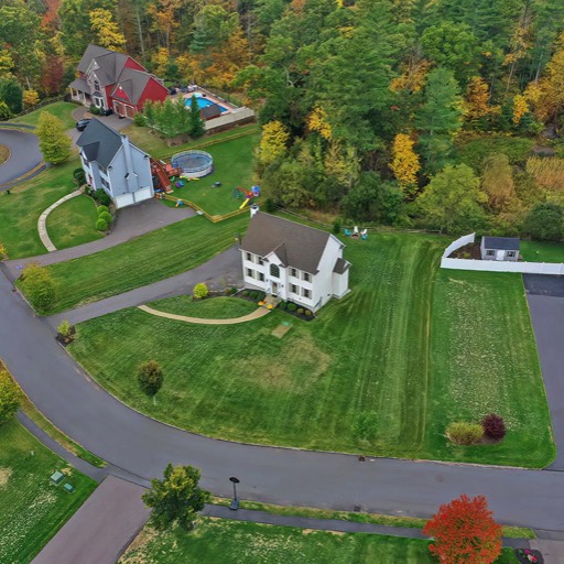 Aerial drone view of a two-story colonial home with lush landscaping